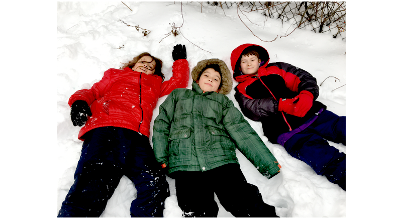three smiling children laying in the snow